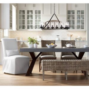 A chandelier hangs from the ceiling in a dining room. The chandelier is made of metal and has a geometric design. The chandelier is surrounded by a dining table, chairs, and a bench.