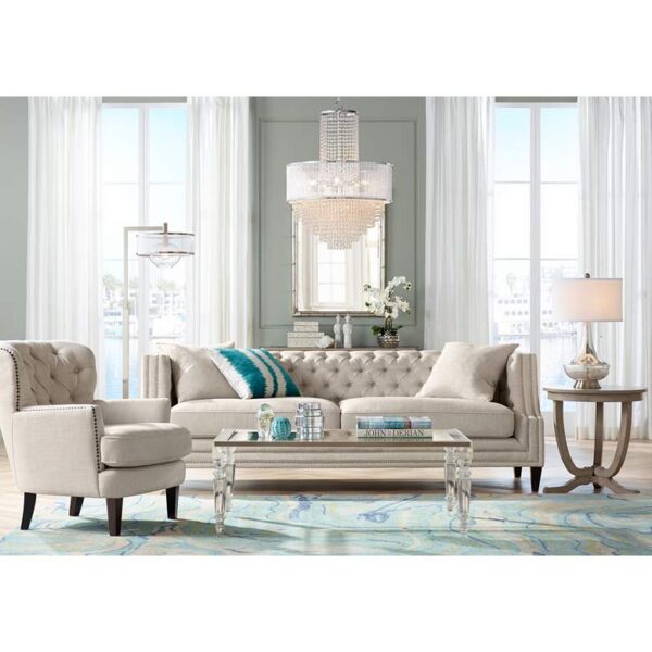 A product image of a living room with a couch, chair, coffee table, and chandelier. The couch is brown and has a floral pattern. The chair is white and has a curved back. The coffee table is made of glass and has a metal frame. The chandelier is made of crystals and has a round base.