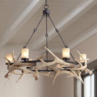 A deer antler chandelier hanging from a ceiling. The chandelier is made of deer antlers and metal. It has 6 lights that are turned on.