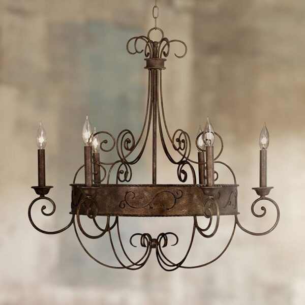 A rustic wrought iron chandelier with six candle sleeves. The chandelier is hanging from a chain and is suspended above a white background. The candles are not burning.