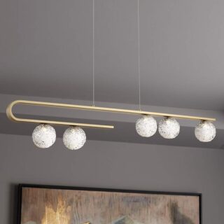 A pendant light hanging from a ceiling next to a painting. The light fixture is made of brushed gold metal and has three clear glass spheres hanging from it. The light is turned on and is emitting a soft, diffused light. The painting is abstract and has a variety of colors and shapes.