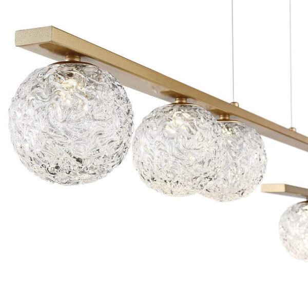 Close-up of a Eurofase Phillimore LED pendant light. The light fixture is made of brushed gold metal and has three clear glass spheres hanging from it. The light is turned on and is emitting a soft, diffused light.